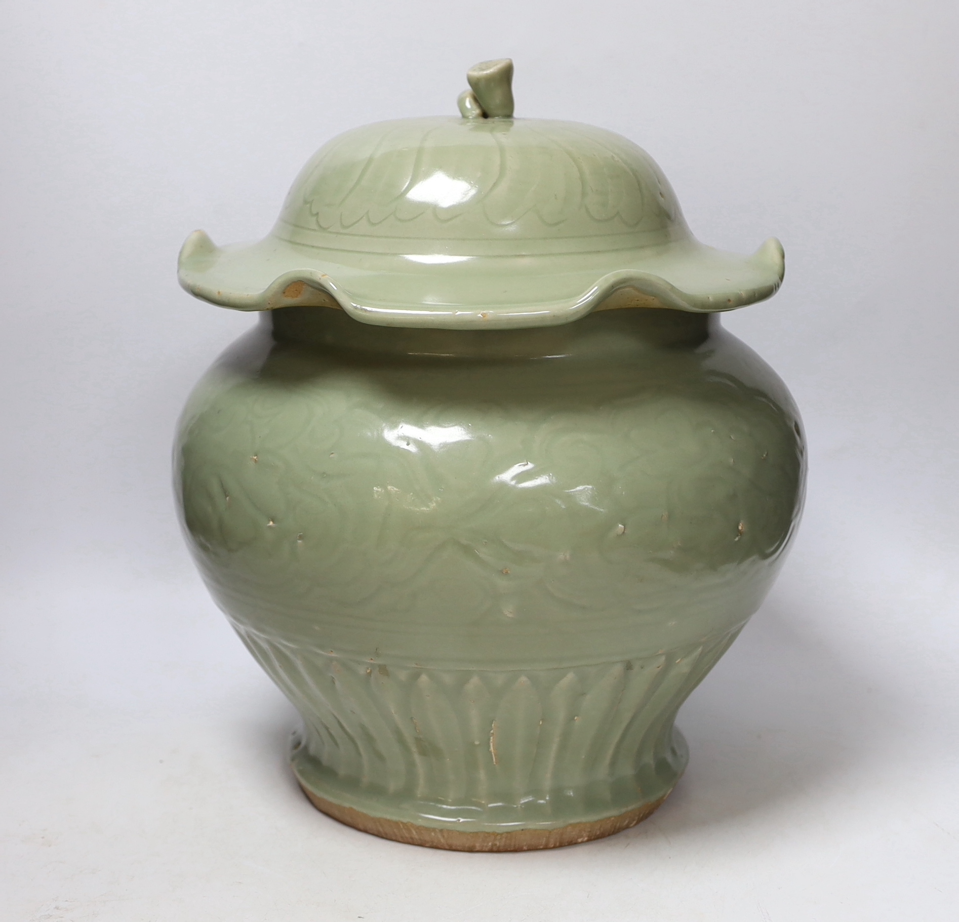 A large Chinese celadon jar and cover, Ming dynasty or later, the lotus leaf shaped cover above a foliate carved baluster body, 35cm high